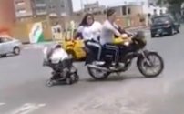Captan a pareja remolcando en motocicleta la carriola con su bebé.